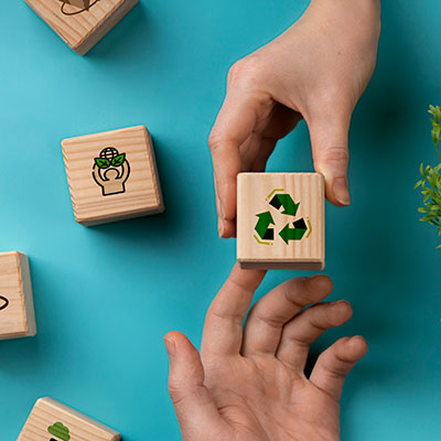 Two hands pass a wooden block with recycling symbol drawn on it.